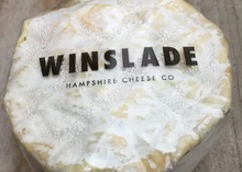A disc of Winslade cheese, wrapped in a white sheet, reveals its cream-colored interior and bloomy rind