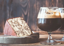 A wedge of Original Irish Porter cheese rests on a round wooden surface, accompanied by a glass of porter wine, all set atop a wooden table