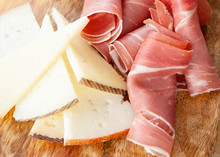 Thin slices of Queso Ibérico and ham elegantly arranged on a wooden board
