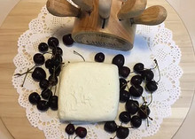 A rectangular piece of Akkawi cheese placed on a white lace paper, accompanied by black currants, all arranged on a wooden board