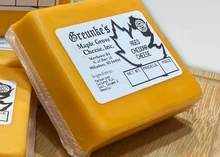 Block of Aged Cheddar wrapped in plastic with label on top, neatly arranged on a wooden table.