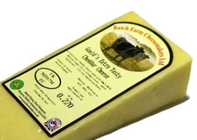 A slice of Farmhouse Extra Tasty Cheddar cheese wrapped in a paper with a label on the top placed against a white background.