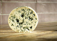 A disc of Fourme d'Ambert cheese showing it cream-coloured paste with prominent blue veins, rests on a wooden surface