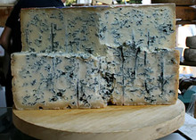 A wheel of Gorgonzola cheese, cut in half and stacked to show its pale cream interior with blue veins throughout, rests on a wooden surface