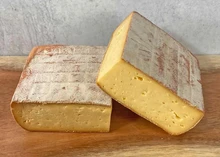 Pieces of Grayson cheese, showcasing a reddish-orange rind and golden interior, arranged on a wooden surface.