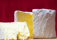 Slices of Kunik Button cheese showcasing white bloomy rind and creamy texture, sit on a wooden surface