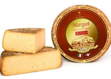 A wheel of Margot cheese with a red label on top, accompanied by wedges that reveal a creamy interior and an inedible rind.