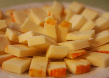 Rectangular slices of Muenster cheese, with a pale yellow interior and orange rind, arranged neatly on a wooden plate