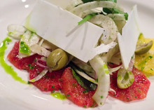 Slices of Ricotta Salata cheese arranged on top of a salad with grapefruit, avocado, and olives