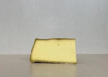 A slice of Appalachian cheese, showcasing its velvety texture and rind, is placed on a wooden surface.