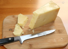 Cheddar cheese cut into pieces on a wooden cutting board, with a cutting knife beside it