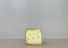 A slice of Chocolate Lab cheese with crushed cocoa nibs on the rind, placed on a wooden surface