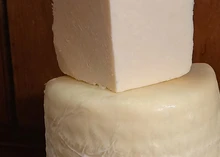 A quarter piece of Coverdale cheese placed on a half-cut wheel of the same cheese, revealing its pale interior, all set against a dark background.