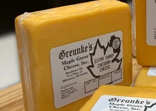 Block of Extra Sharp Cheddar, wrapped in plastic with label rests on a wooden table.