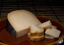 A large slice of Gouda, accompanied by small pieces placed on crusty bread, all arranged on a wooden plate