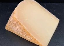 A slice of Lord of the Hundreds cheese, showcasing its natural rind and creamy texture, rests on black marble