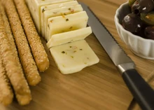 Sliced Pepper Jack cheese with sesame seed breadsticks, Mediterranean olives, and hot peppers on a wooden cheese board, with a knife