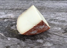 A slice of Pecorino Rocco cheese showcasing its red rind and smooth texture rests on a wooden surface