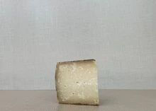 A slice of Providence cheese showcasing its pale yellow interior placed on a wooden surface