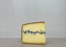 A slice of Ridgeline cheese, revealing its dark rind and pale yellow interior with a dark vein of vegetable ash streaking through the middle