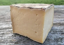 A large slice of Single Gloucester cheese revealing its ivory interior placed on a wooden surface