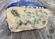 A slice of Strathdon Blue cheese, showcasing its blue veining, rests on a wooden surface