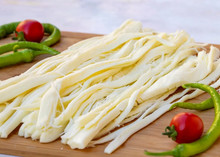 The image shows thin, long slices of String cheese, two red tomatoes, and several long green peppers, all on a wooden board