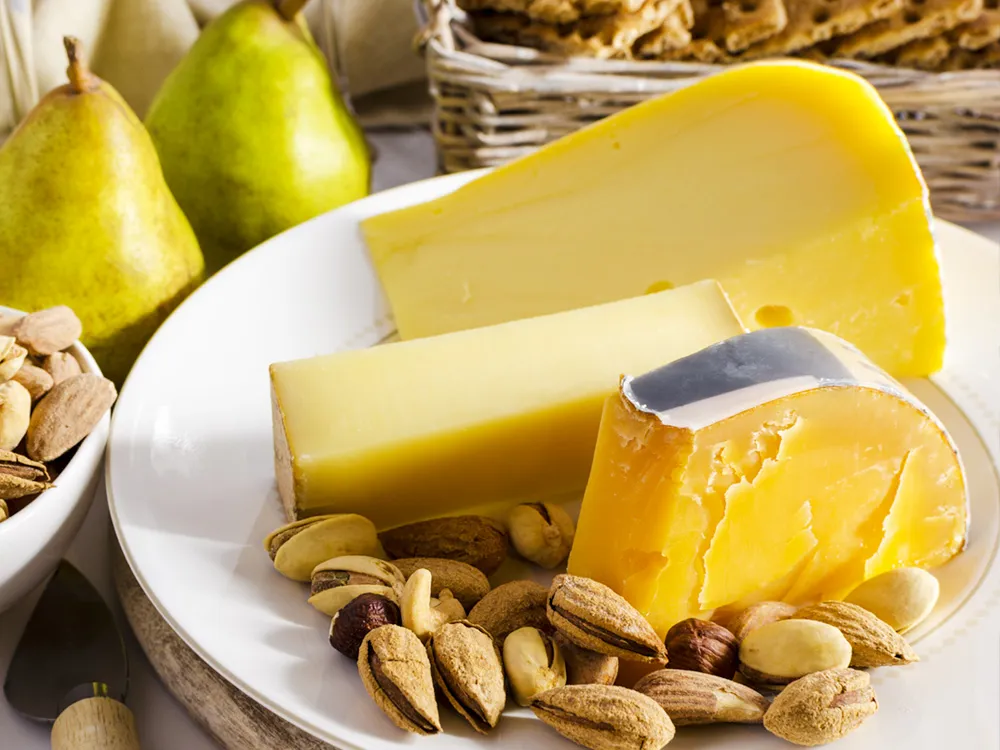 Slices of Beemster Classic cheese arranged with nuts in a plate, accompanied with pears and nuts.