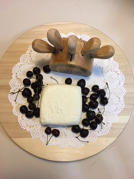 A rectangular piece of Akkawi cheese placed on a white lace paper, accompanied by black currants, all arranged on a wooden board