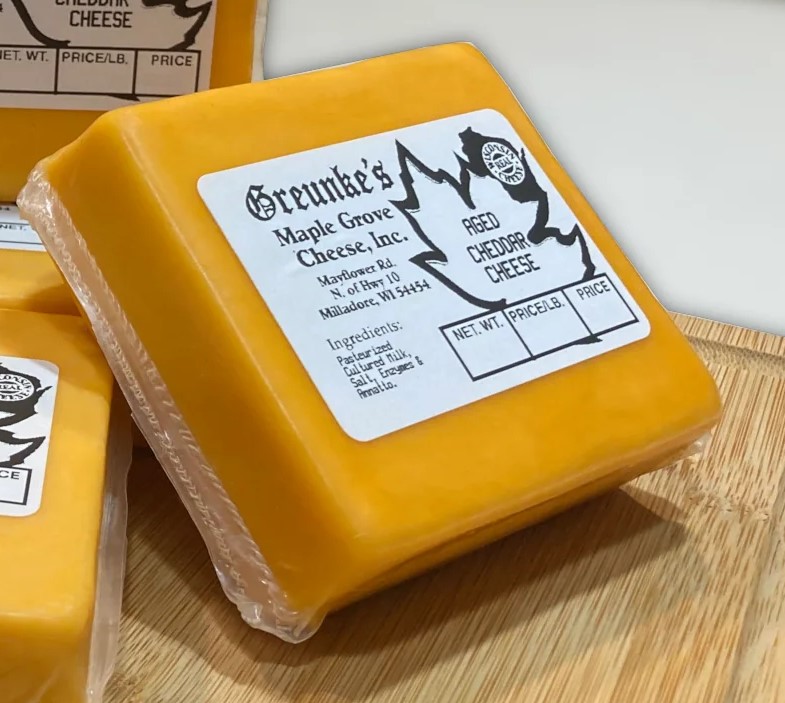 Block of Aged Cheddar wrapped in plastic with label on top, neatly arranged on a wooden table.