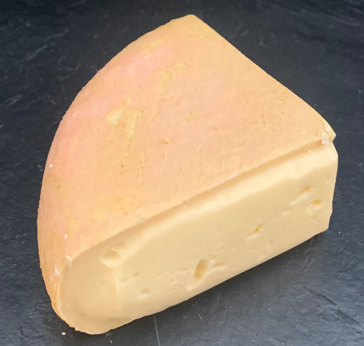 A triangular slice of Burwash Rose cheese sits on a black marble