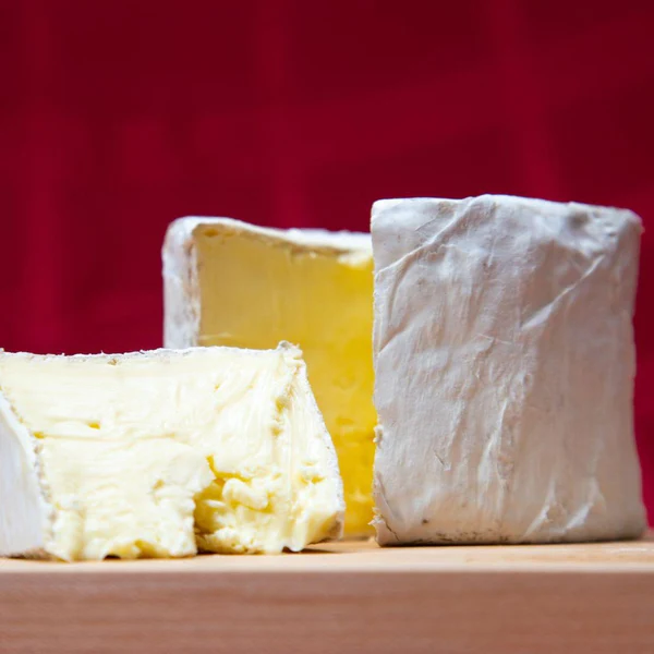 Slices of Kunik Button cheese showcasing white bloomy rind and creamy texture, sit on a wooden surface