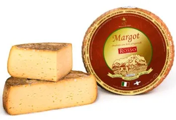 A wheel of Margot cheese with a red label on top, accompanied by wedges that reveal a creamy interior and an inedible rind.