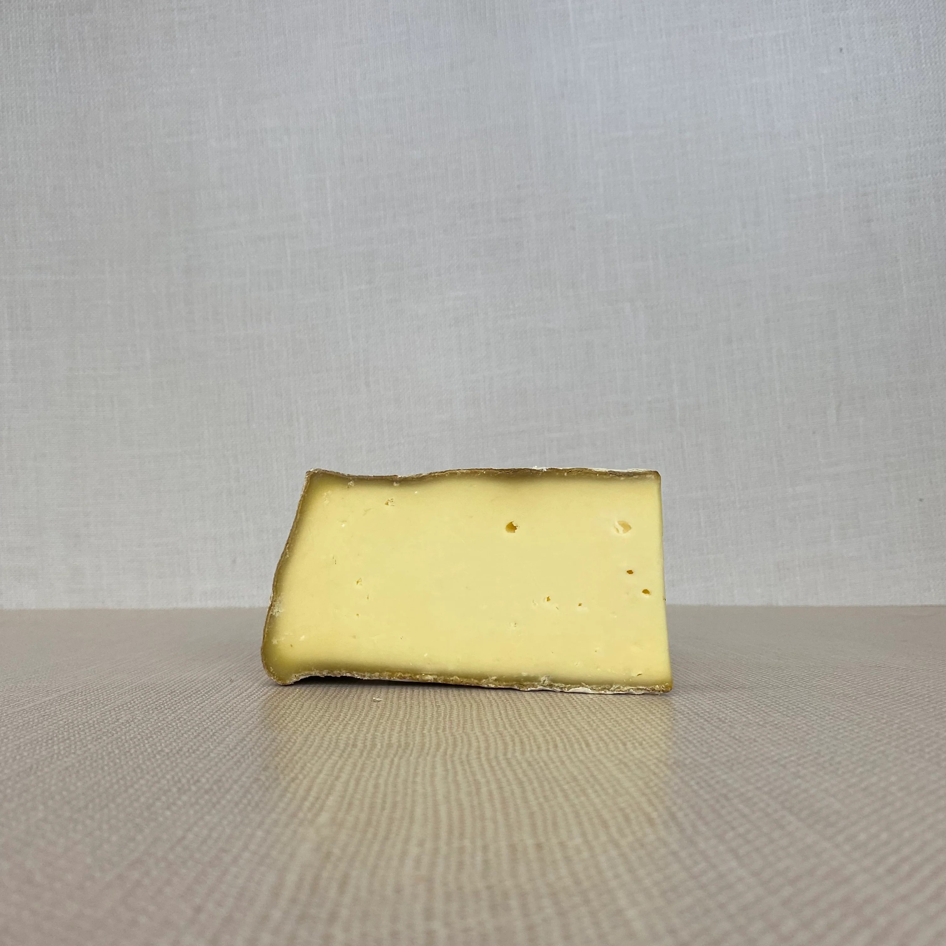 A slice of Appalachian cheese, showcasing its velvety texture and rind, is placed on a wooden surface.