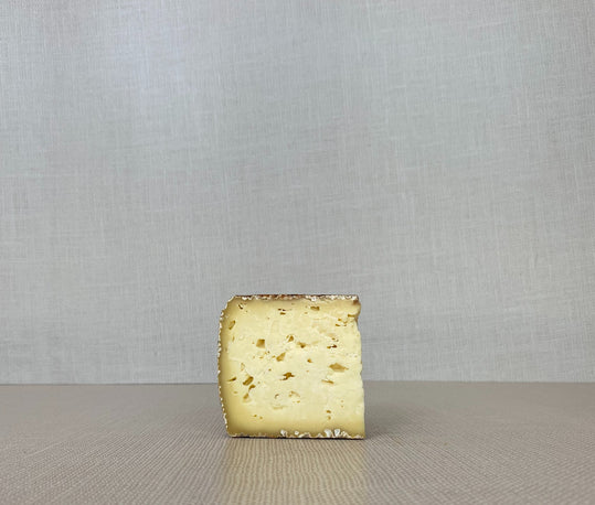 A slice of Chocolate Lab cheese with crushed cocoa nibs on the rind, placed on a wooden surface