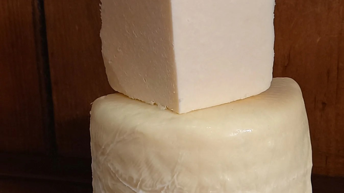 A quarter piece of Coverdale cheese placed on a half-cut wheel of the same cheese, revealing its pale interior, all set against a dark background.