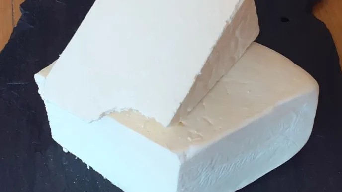 Wedges of Crumbly Lancashire cheese stacked showcasing white birght interior, placed on a black surface