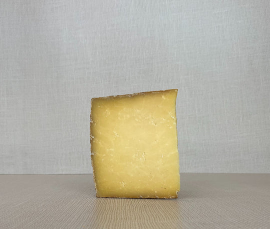 A slice of Drovers Road cheddar showcasing its yellow interior placed on a wooden surface
