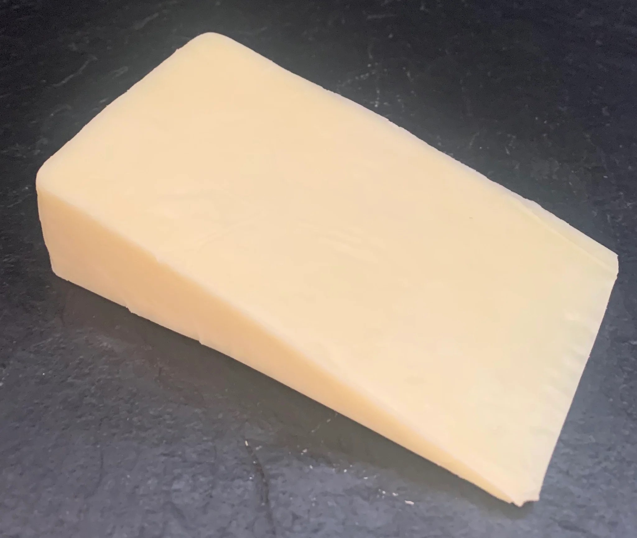 A slice of Duddleswell cheese, showcasing its creamy texture, rests on black marble