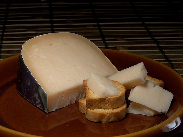 A large slice of Gouda, accompanied by small pieces placed on crusty bread, all arranged on a wooden plate