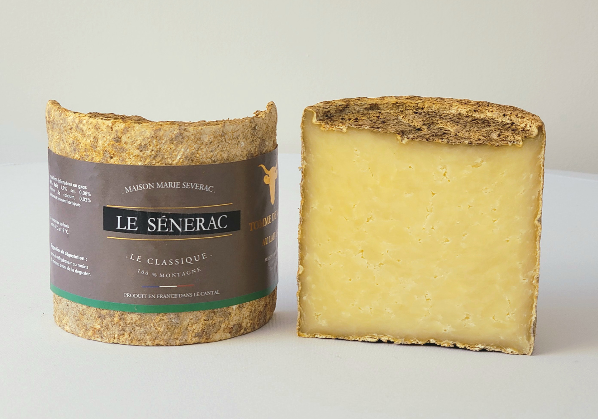 A halved cylindrical Le Sanerac cheese, featuring a delicate whitish rind and a rich yellow interior, is set against a grey background.