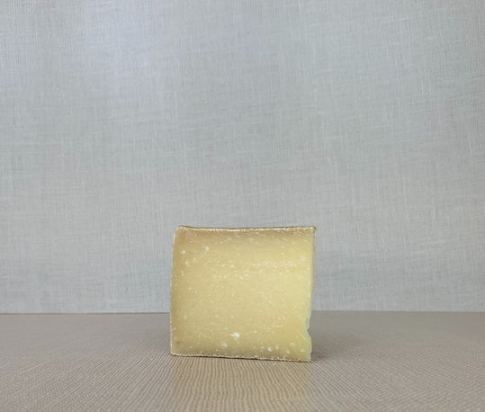 A slice of Lindale cheese with its pale yellow interior, placed on a wooden surface.