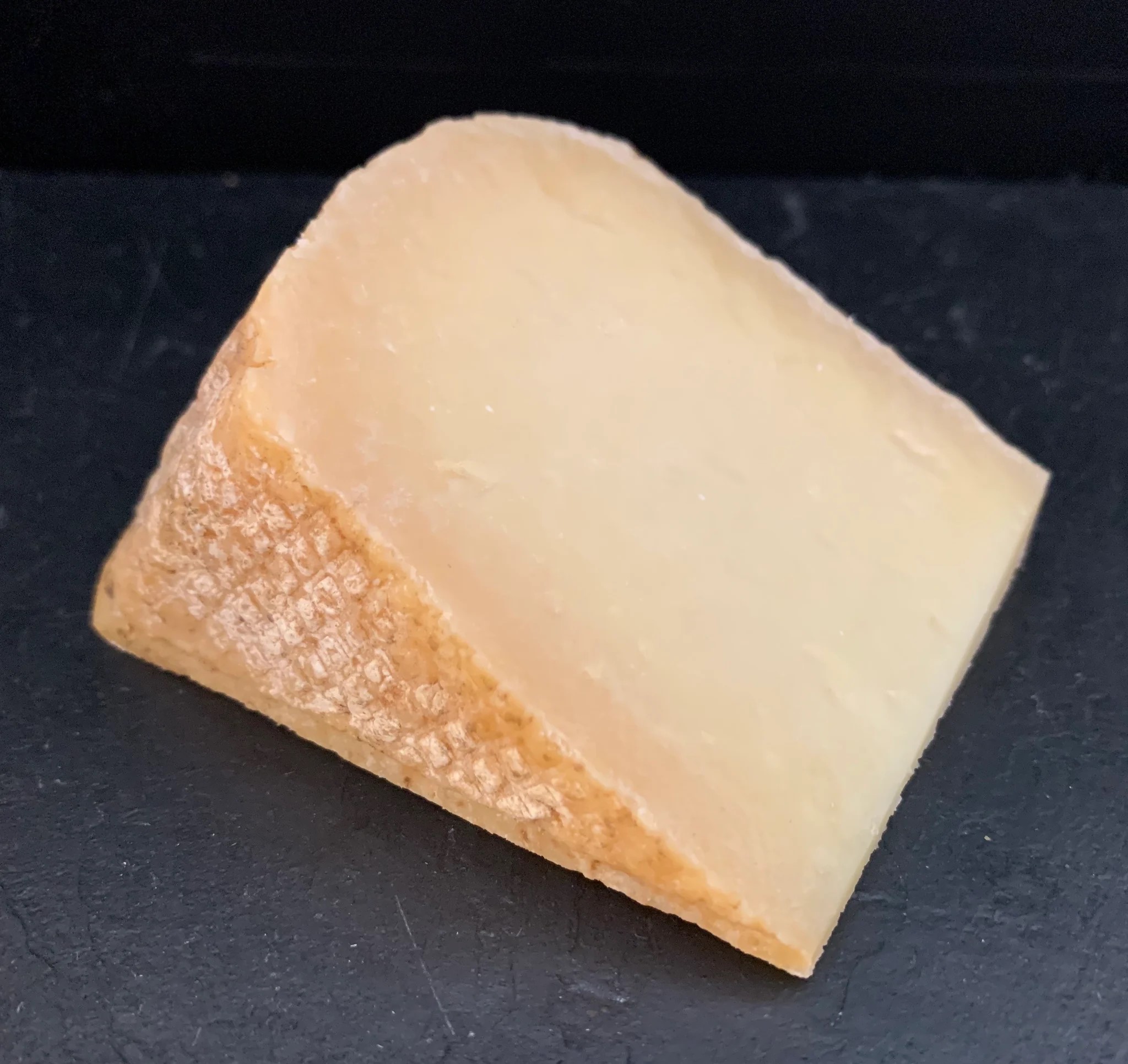 A slice of Lord of the Hundreds cheese, showcasing its natural rind and creamy texture, rests on black marble
