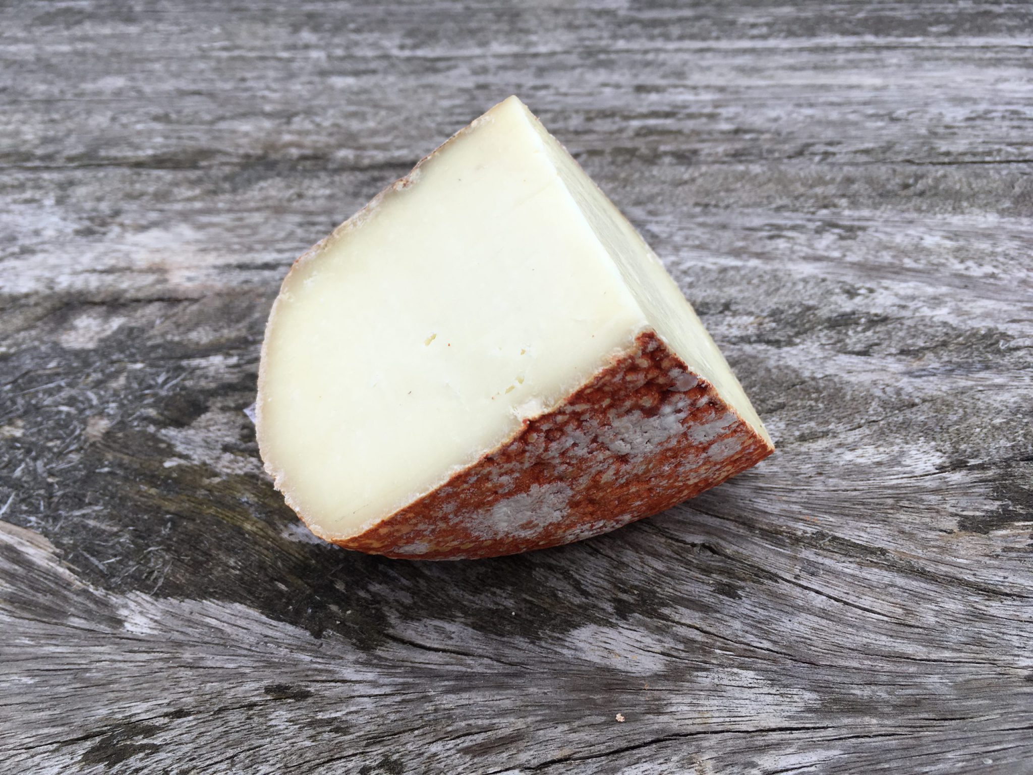 A slice of Pecorino Rocco cheese showcasing its red rind and smooth texture rests on a wooden surface