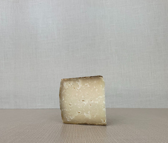 A slice of Providence cheese showcasing its pale yellow interior placed on a wooden surface