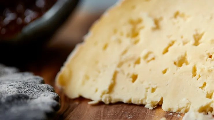 A large piece of Sharpham Rustic cheese rests of a wooden surface