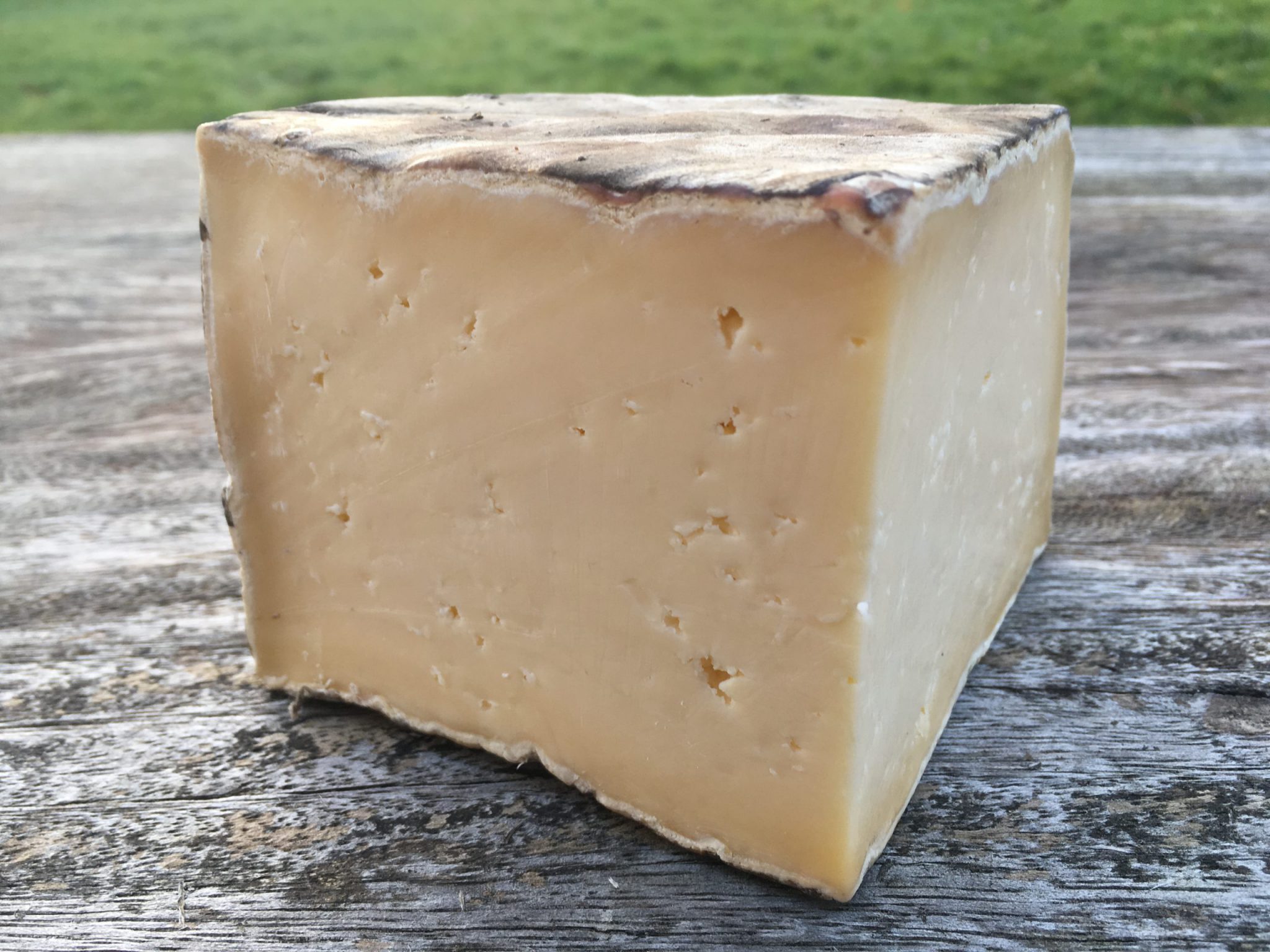 A large slice of Single Gloucester cheese revealing its ivory interior placed on a wooden surface