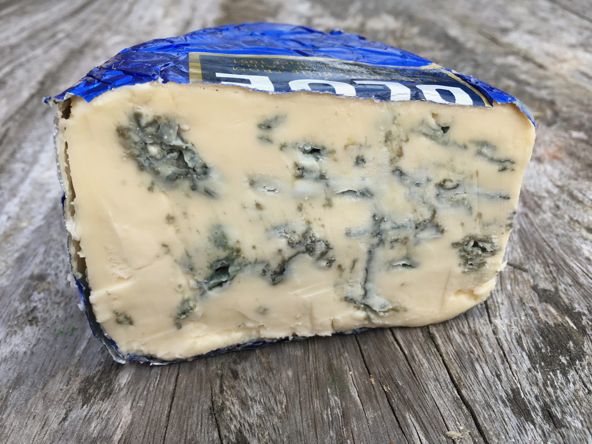 A slice of Strathdon Blue cheese, showcasing its blue veining, rests on a wooden surface